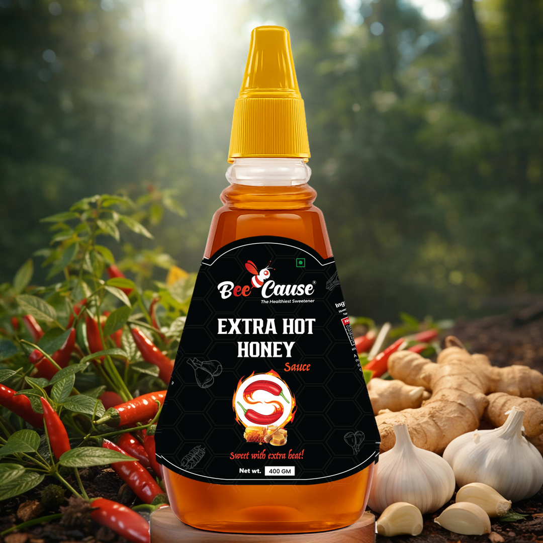 A squeeze bottle of Bee Cause Extra Hot Honey Sauce, labeled "Sweet with extra heat!", sitting on a wooden surface with fresh red chilies, ginger root, and garlic bulbs in a natural outdoor setting.