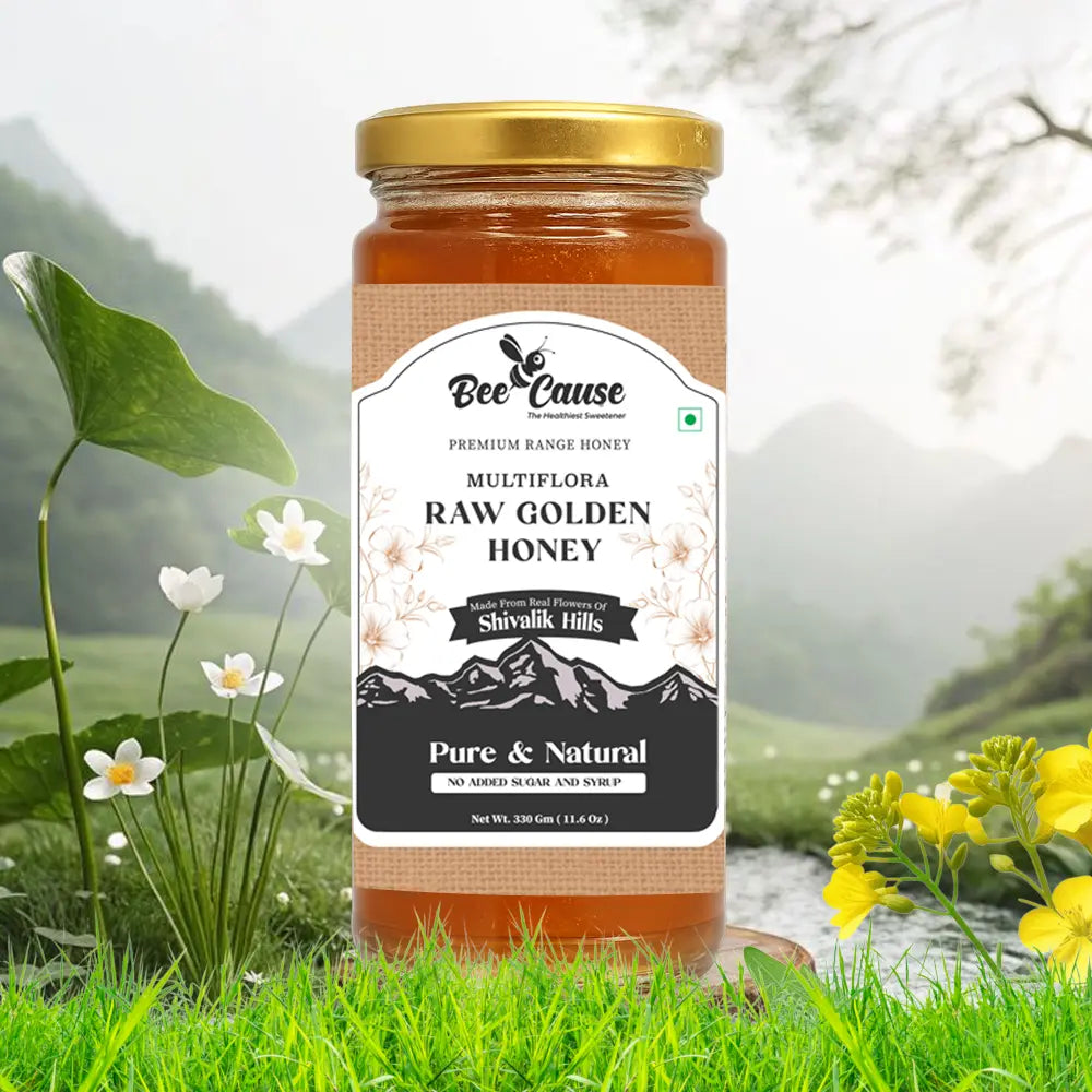 A single jar of Bee Cause Multiflora Raw Golden Honey sitting on a grassy bank next to a small stream, surrounded by white and yellow wildflowers.