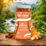 A jar of Bee Cause Skim Blend of Honey is displayed on a rustic wooden table with ingredients like cinnamon sticks, ginger, and a small bottle of honey, set against a blurred natural forest background.