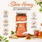 A jar of Bee Cause Skim Honey centered on a light cream background with decorative honeycomb props, ginger, an apple, and text callouts about ACV, cinnamon, ginger, premium quality, no added sugar, no chemicals, and natural ingredients.