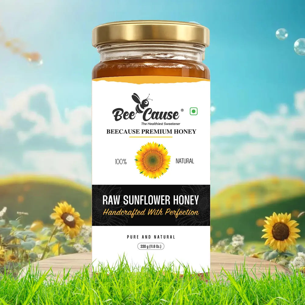 A jar of Bee Cause Raw Sunflower Honey featuring a bright yellow sunflower illustration on the label, positioned on a wooden surface in a sunny field of sunflowers under a blue sky.