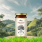 A scenic product display of Bee Cause Sidr Honey set against a lush green hill and blue sky background, emphasizing its natural and wild origin.