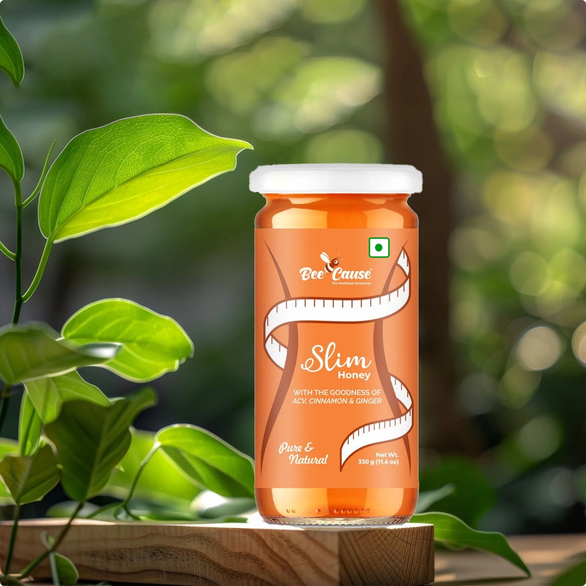 A scenic product shot of Bee Cause Slim Honey placed on a wooden block, surrounded by fresh green leaves and a blurred forest background to emphasize its natural ingredients.