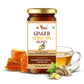A bottle of Ginger Curcumin Honey surrounded by fresh ginger root, raw honeycomb, and a cup of warm tea, illustrating the natural ingredients and serving suggestion.