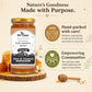 A jar of Bee Cause Raw Golden Honey displayed on a wooden slice with honeycomb and a honey dipper, alongside promotional text about hand-packed care and empowering communities on a warm beige background.