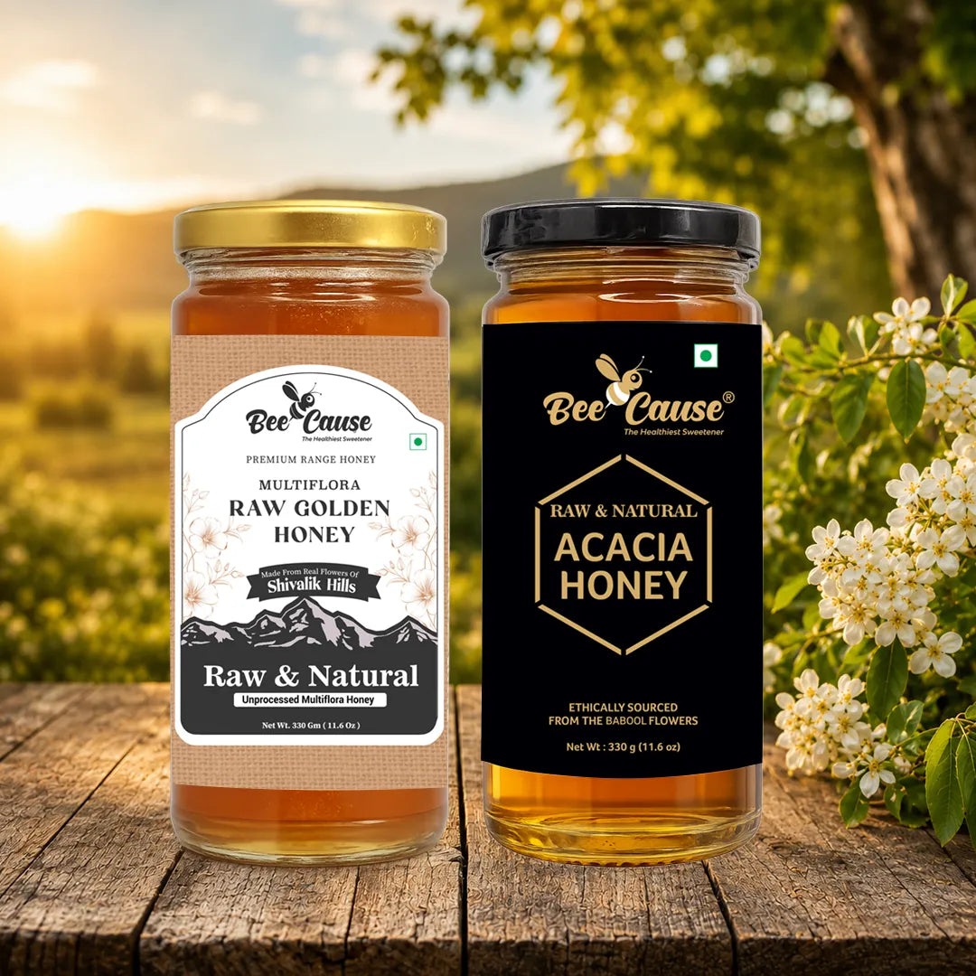 Two glass jars of Bee Cause honey displayed side by side on a rustic wooden table. The left jar contains Multiflora Raw Golden Honey with a gold lid and beige label, and the right jar contains Raw & Natural Acacia Honey with a black lid and black label.