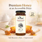 A jar of Bee Cause Sidr Honey is centered against a warm, softly blurred background with honey dripping, a cup of tea, and honeycombs. Text above reads 'Premium Honey at an Accessible Price' and '330g Sidr Honey', with 'Sidr Blossom Raw Unprocessed' at the bottom.