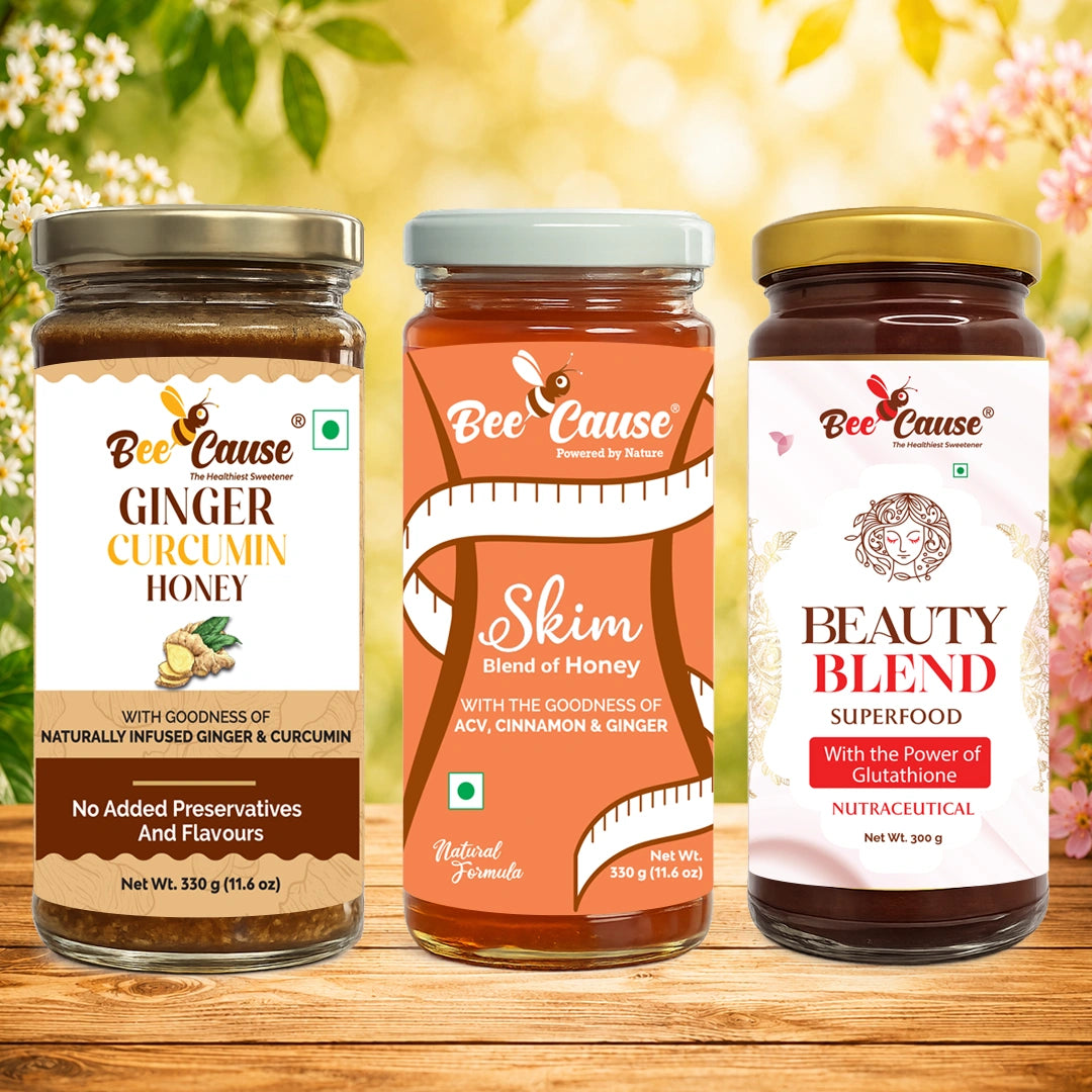Three jars of Bee Cause superfoods and honey displayed side-by-side on a wooden surface with a soft-focus floral background. The products are: Bee Cause Ginger Curcumin Honey, Bee Cause Skim Blend of Honey, and Bee Cause Beauty Blend Superfood.